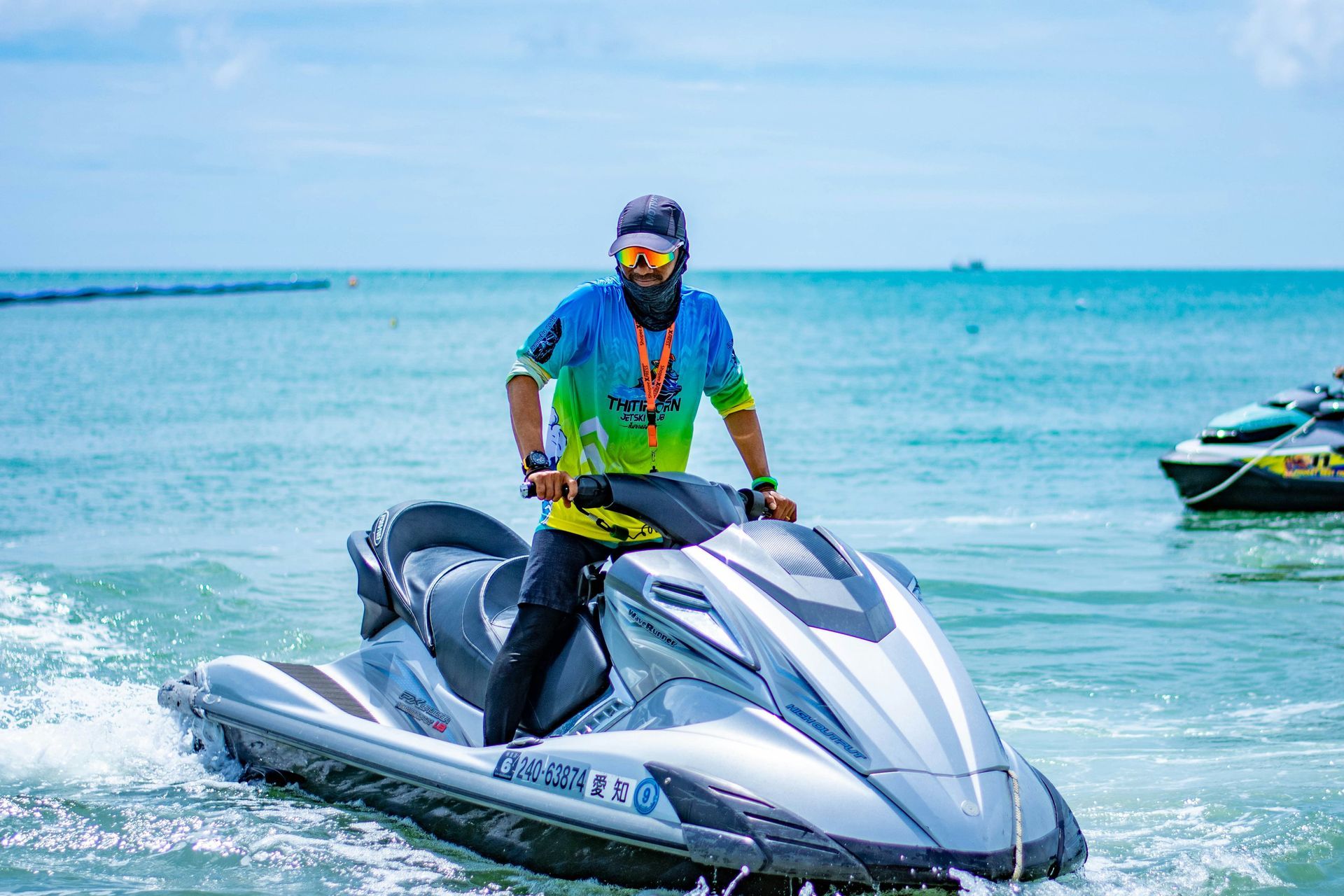 Person riding a white jet ski on blue water, wearing a blue shirt and helmet with reflective goggles.