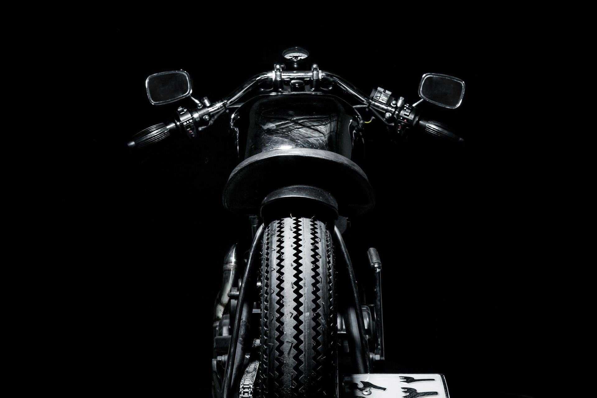 Front view of a black motorcycle on a dark background, with handlebars and mirrors visible