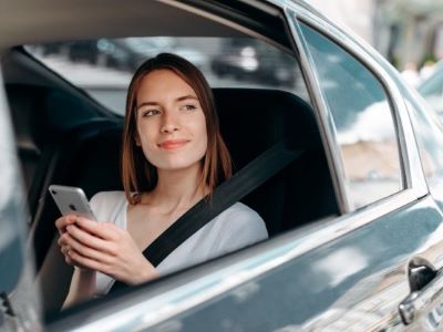 Woman smiling and holding a phone while seated in a car with a seat belt on