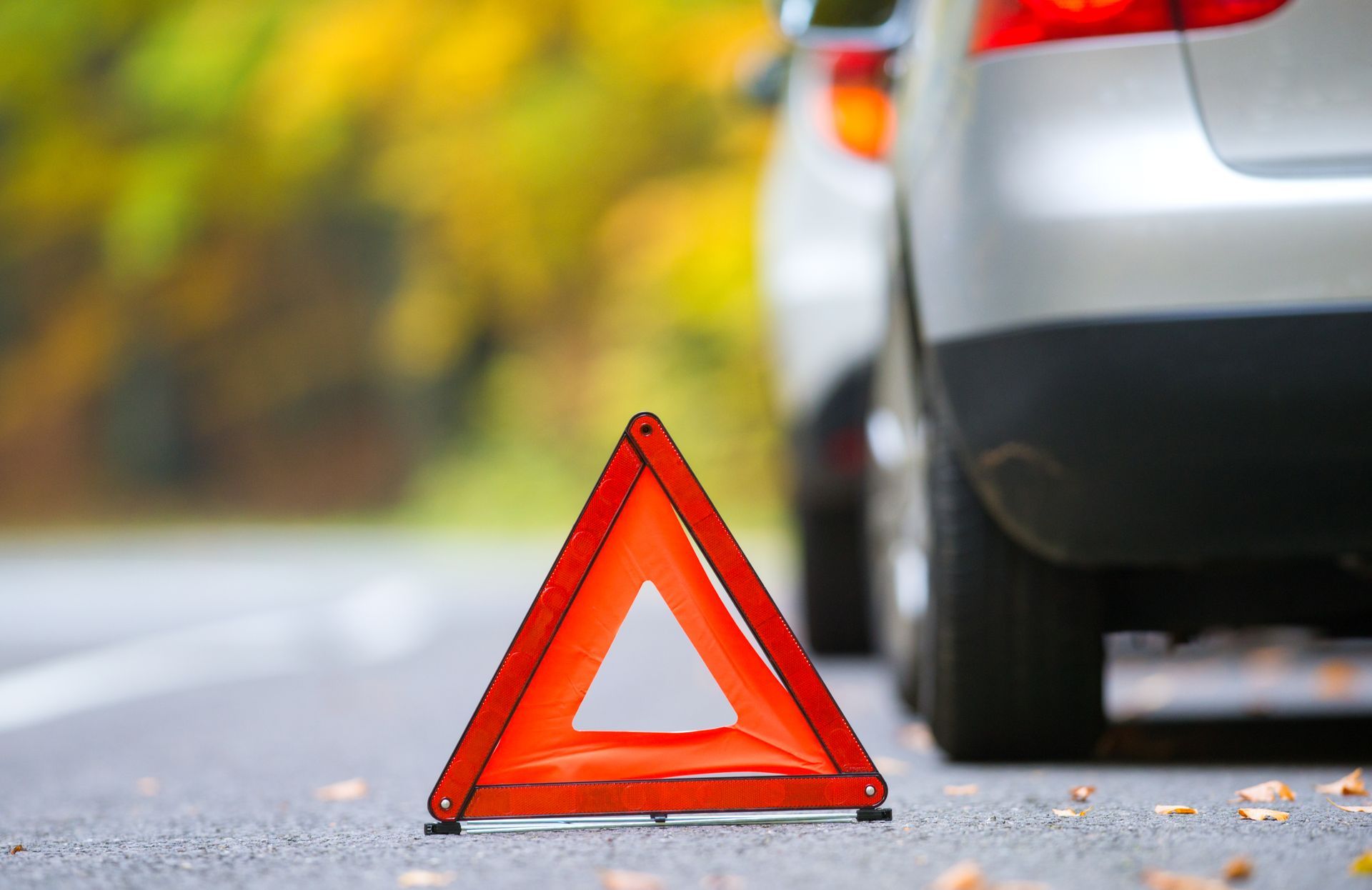 Red roadside warning triangle beside a parked silver car on a blurred road.
