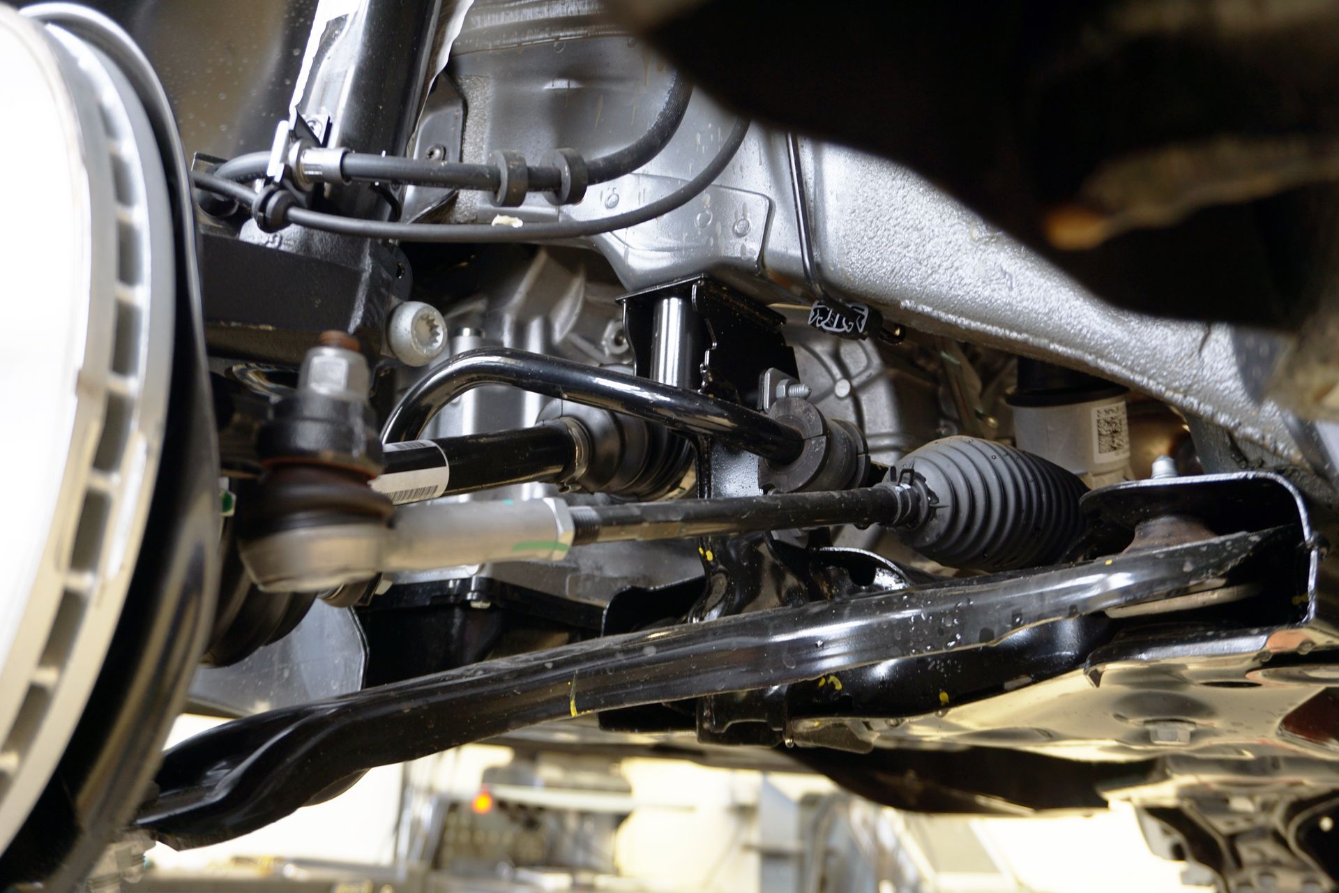 Close-up of a car’s front suspension and steering components under the vehicle.