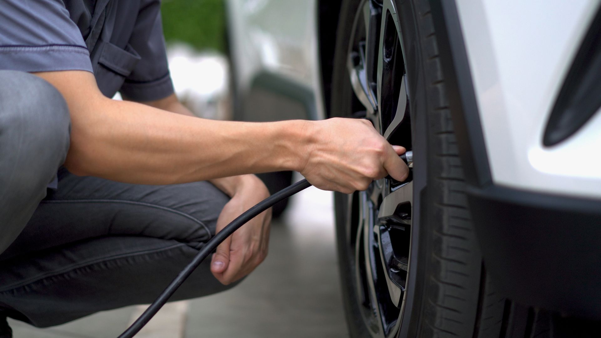 Person inflating a car tire with a handheld air hose beside a white vehicle