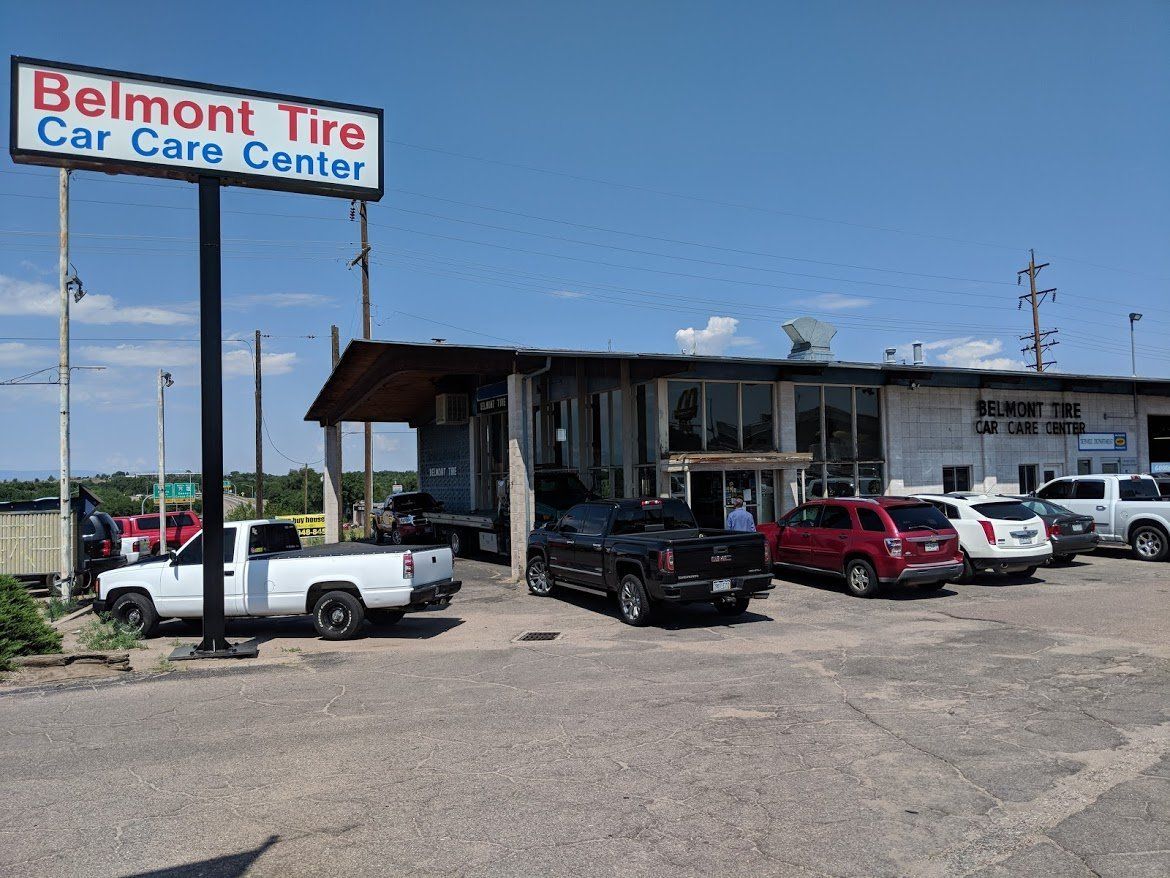 Belmont Tire Car Care Center storefront with parked trucks and cars under a blue sky