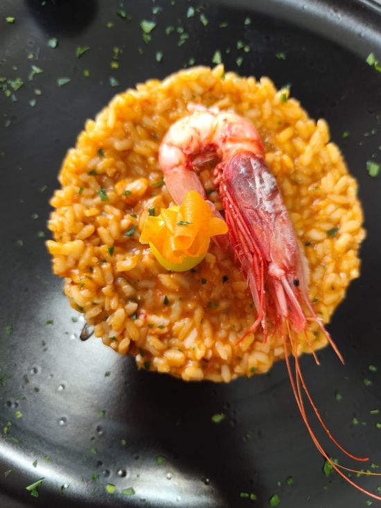 Risotto con gamberi e guarnizione decorativa di pomodoro su un piatto nero, con prezzemolo.
