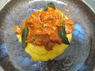 Polenta condita con sugo di carne e pomodoro, guarnita con salvia, in una ciotola con il bordo blu.