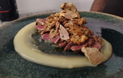 Carne affettata con guarnizione al tartufo su un letto di purea, servita su un piatto verde acqua.