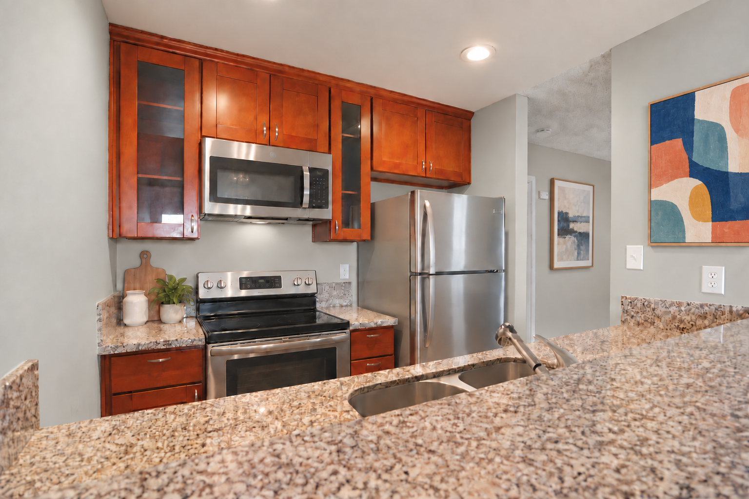 Modern kitchen with granite counters, stainless steel appliances, wood cabinets, and colorful wall art.