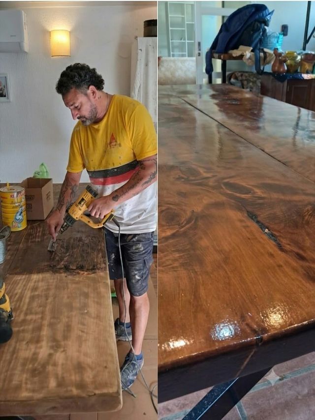 Un hombre lija la superficie brillante de una mesa de madera en un taller, con herramientas a su alcance.