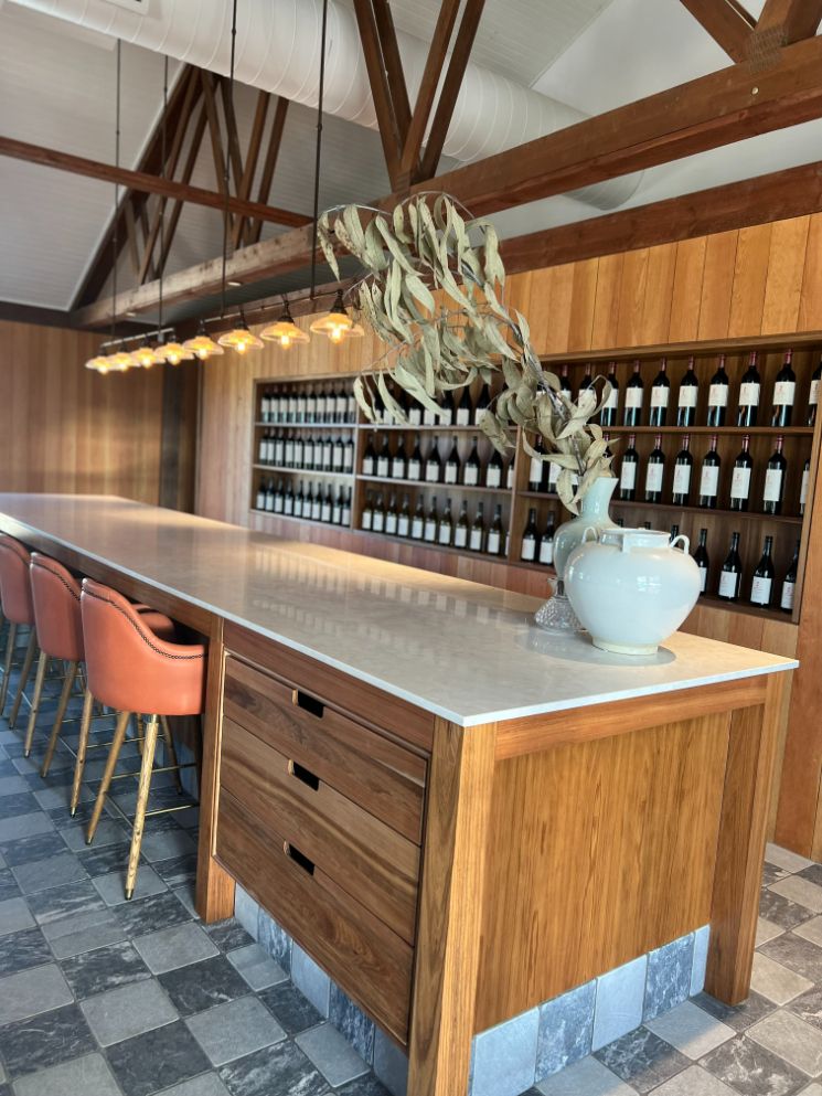 A Long Wooden Table With A Vase On Top Of It In A Room Filled With Bottles Of Wine — Logic Joinery In Fountaindale, NSW