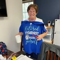 A person smiles while holding up a blue T-shirt that says 