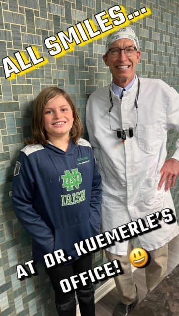 A child wearing a Notre Dame hoodie and a dentist in a white coat smile together in a dental office.