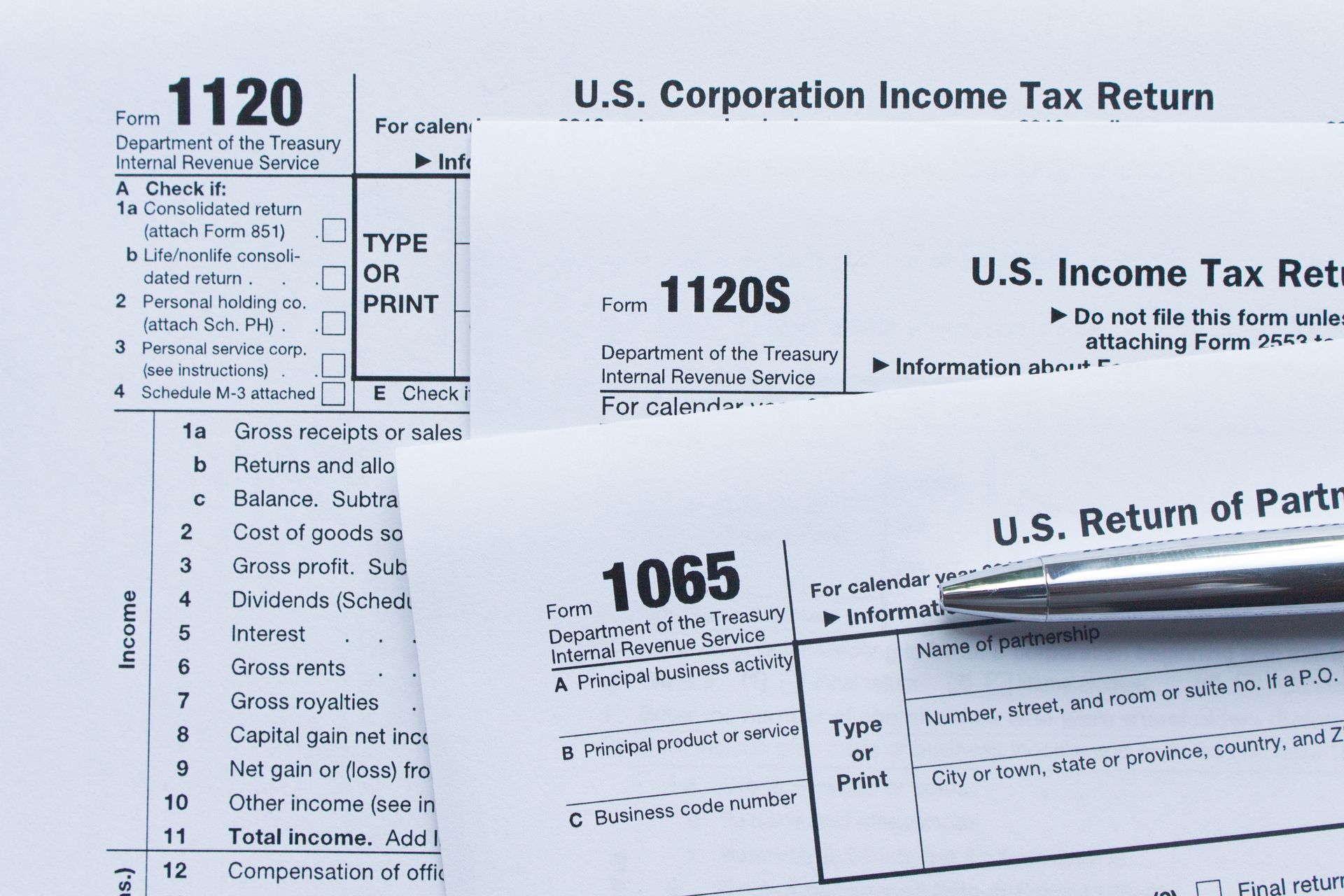 IRS tax forms 1120, 1120S, and 1065 with pen for business tax filing.