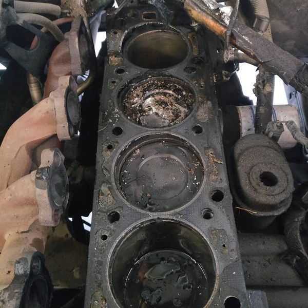 Top view of a worn engine block with three piston cylinders and oily, rusted parts | Auto Pros