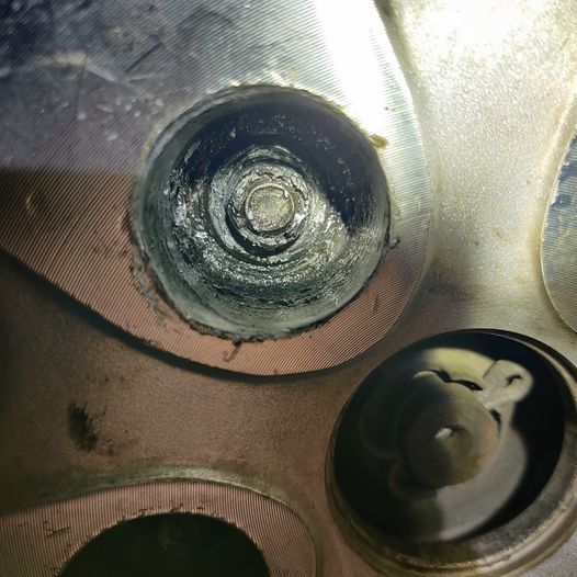 Close-up of metallic mechanical parts, including a circular bolt and a dark recessed opening. | Auto Pros