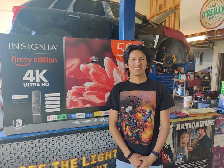 Person smiling in a garage beside an Insignia Fire TV Edition 4K Ultra HD box and a lifted truck. | Auto Pros