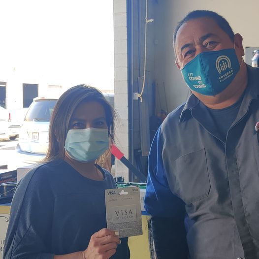 Two people wearing masks stand indoors; one holds up a card toward the camera. | Auto Pros