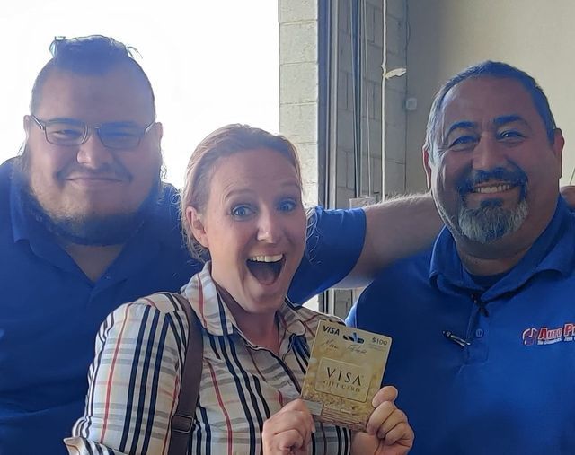 Three people smiling indoors, with the center person holding up a visa document. | Auto Pros