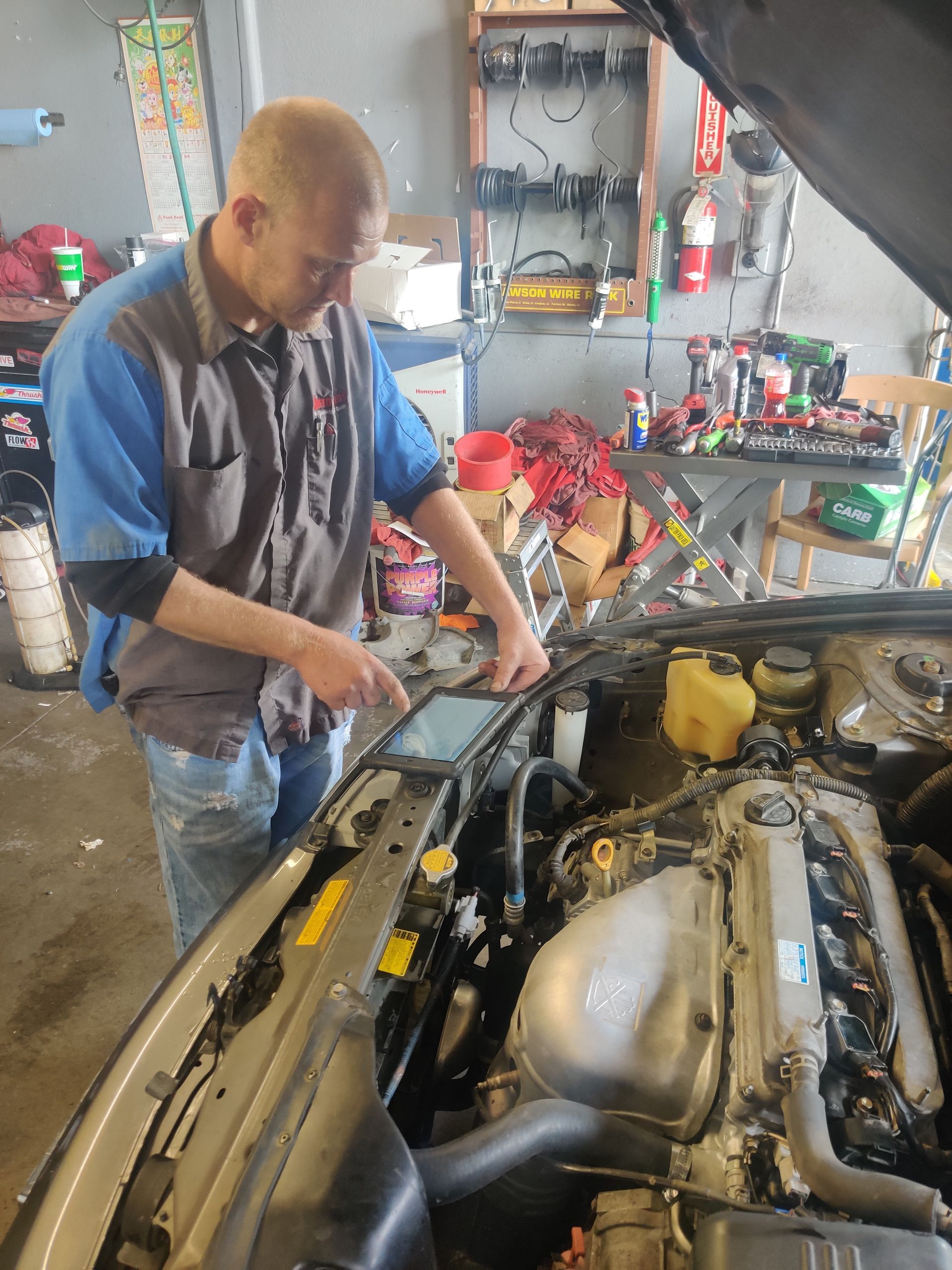 Mechanic working under the hood of a car in a cluttered auto garage | Auto Pros