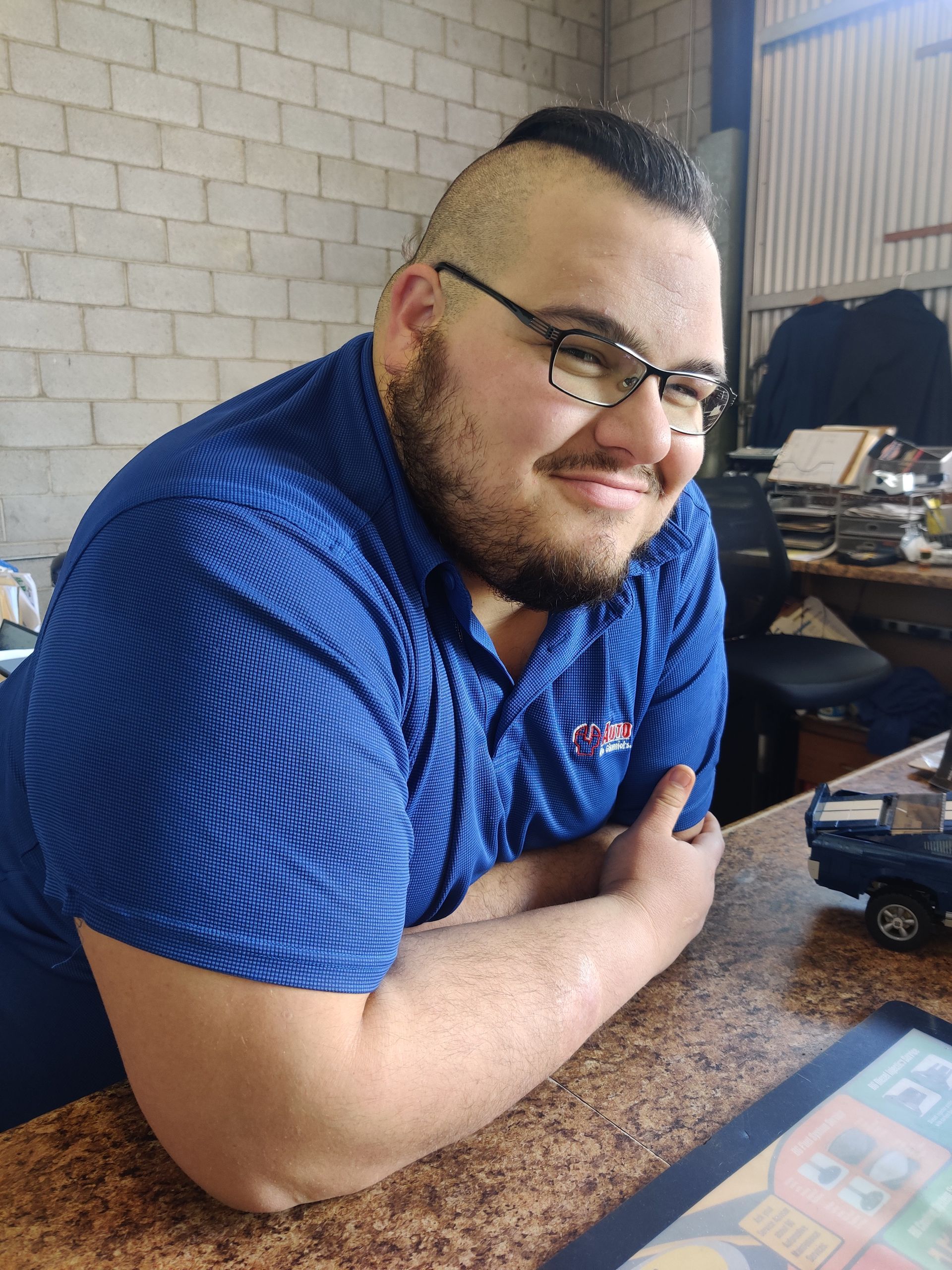 Man in a blue shirt smiling at a table in a casual indoor setting | Auto Pros