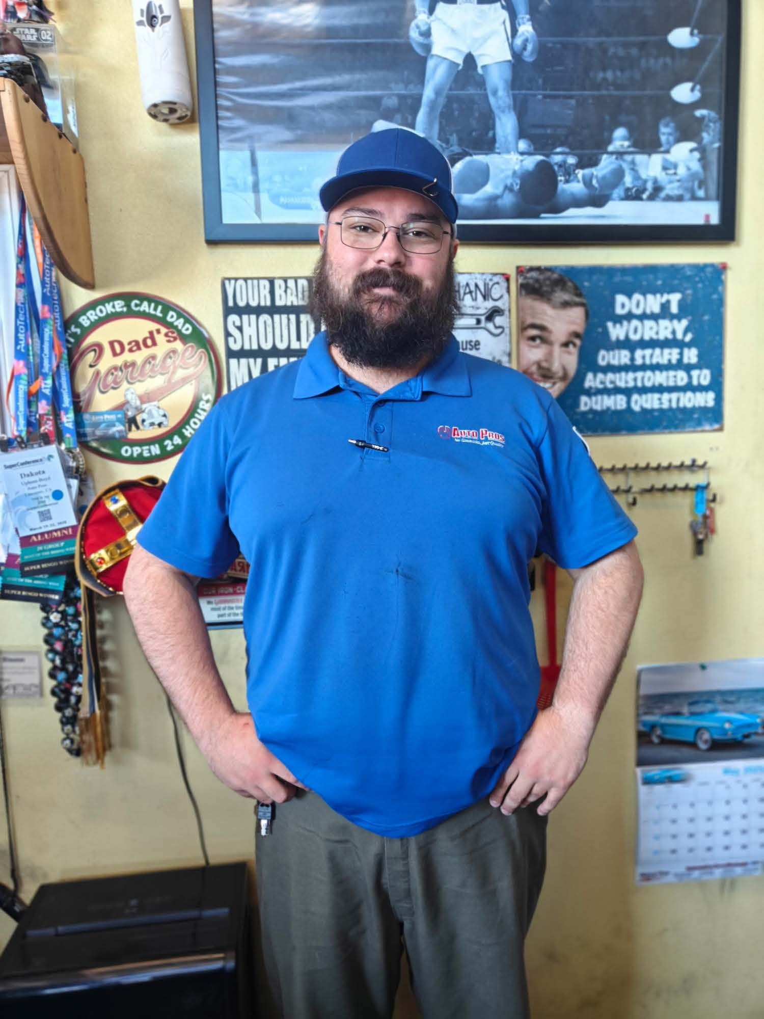 Man in blue polo and cap standing in a room with vintage signs and photos on the wall | Auto Pros