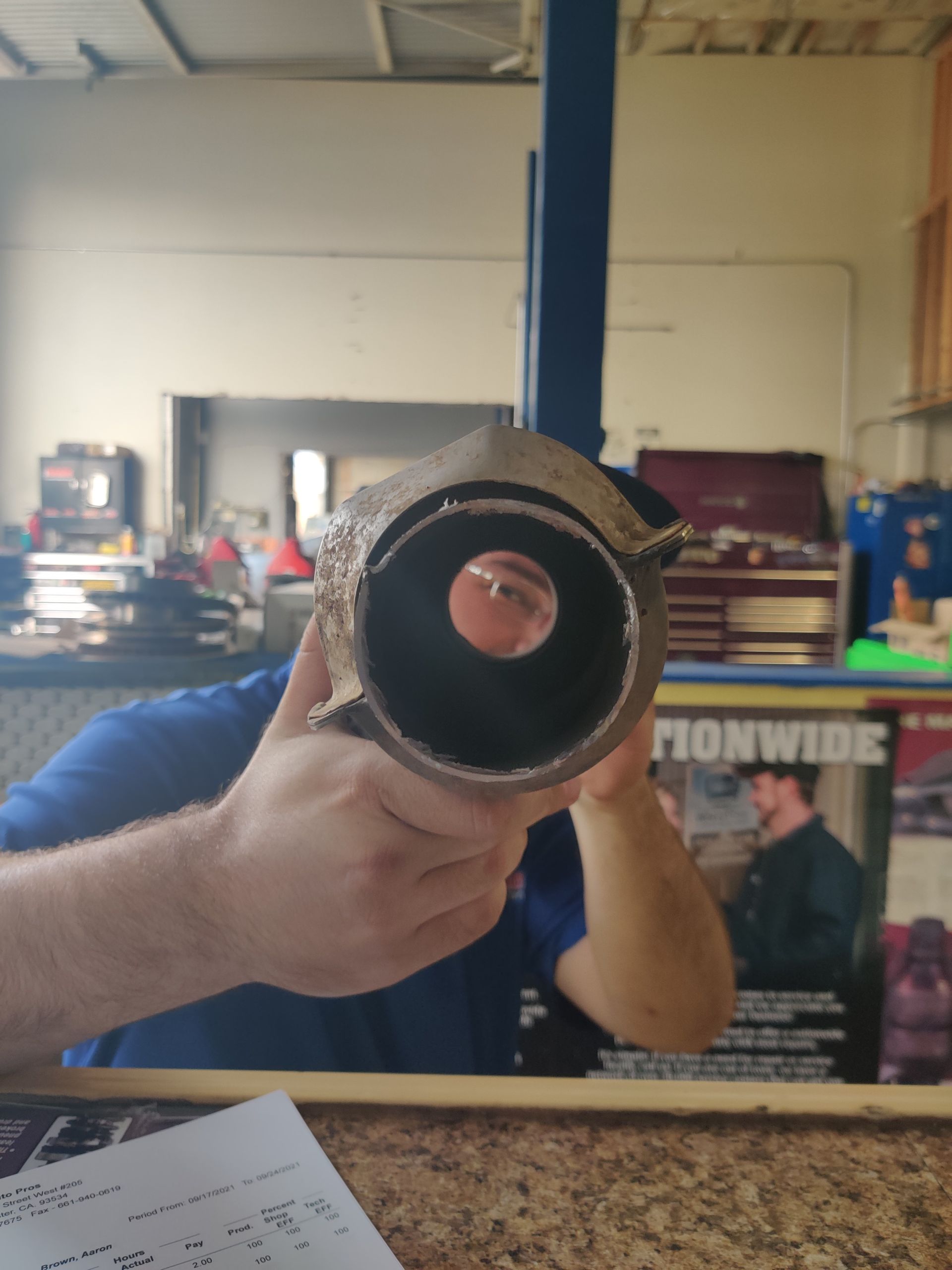Person holding a pipe toward the camera in a workshop or garage, with tools and equipment in the background. | Auto Pros