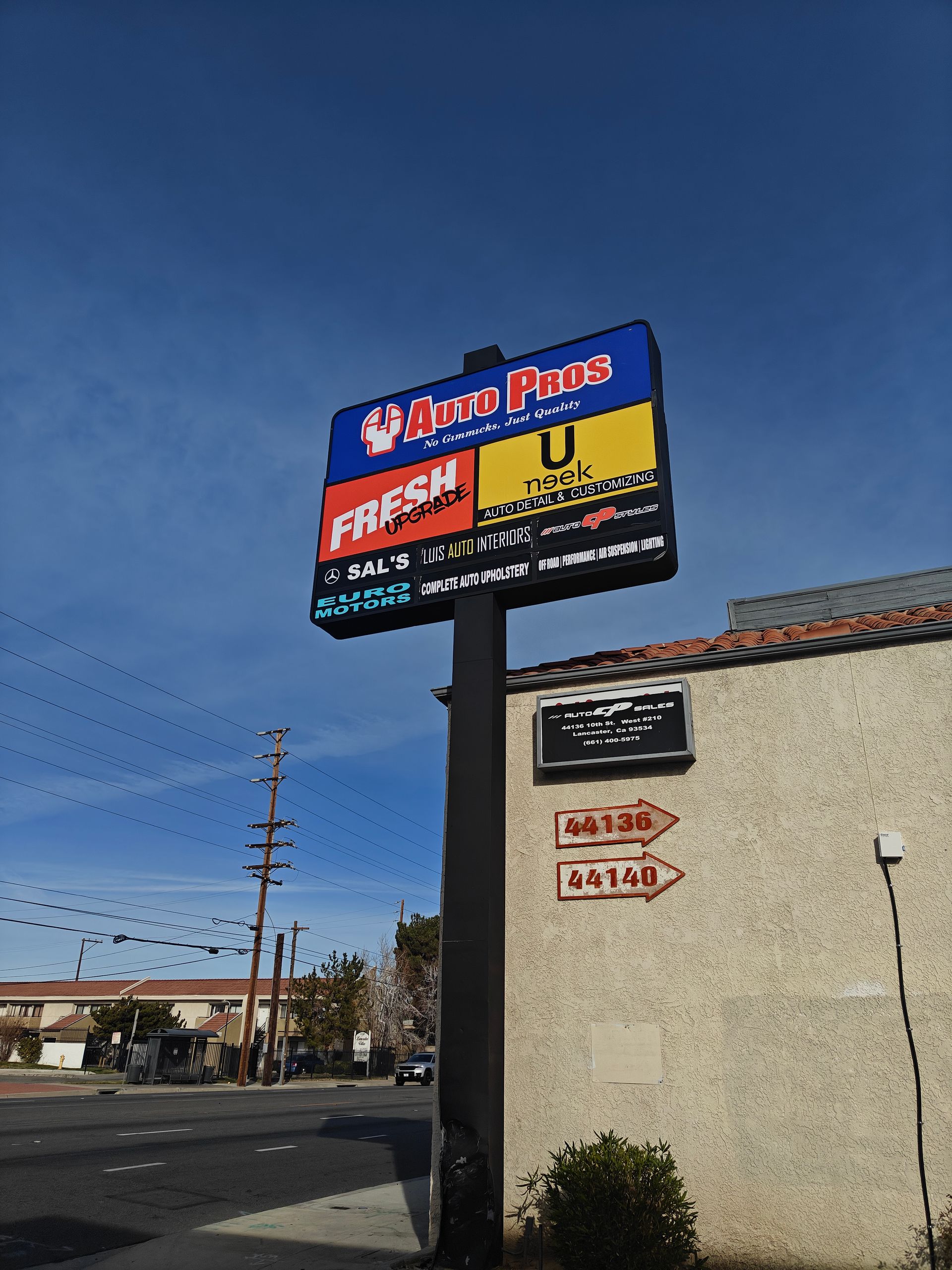 Street view of a pizza restaurant sign on a pole beside a beige building under a clear blue sky | Auto Pros