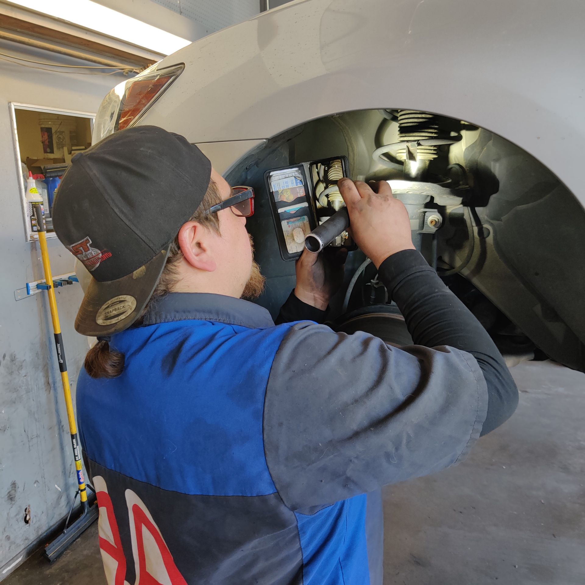 Mechanic inspecting a car wheel well with a phone in a garage | Auto Pros