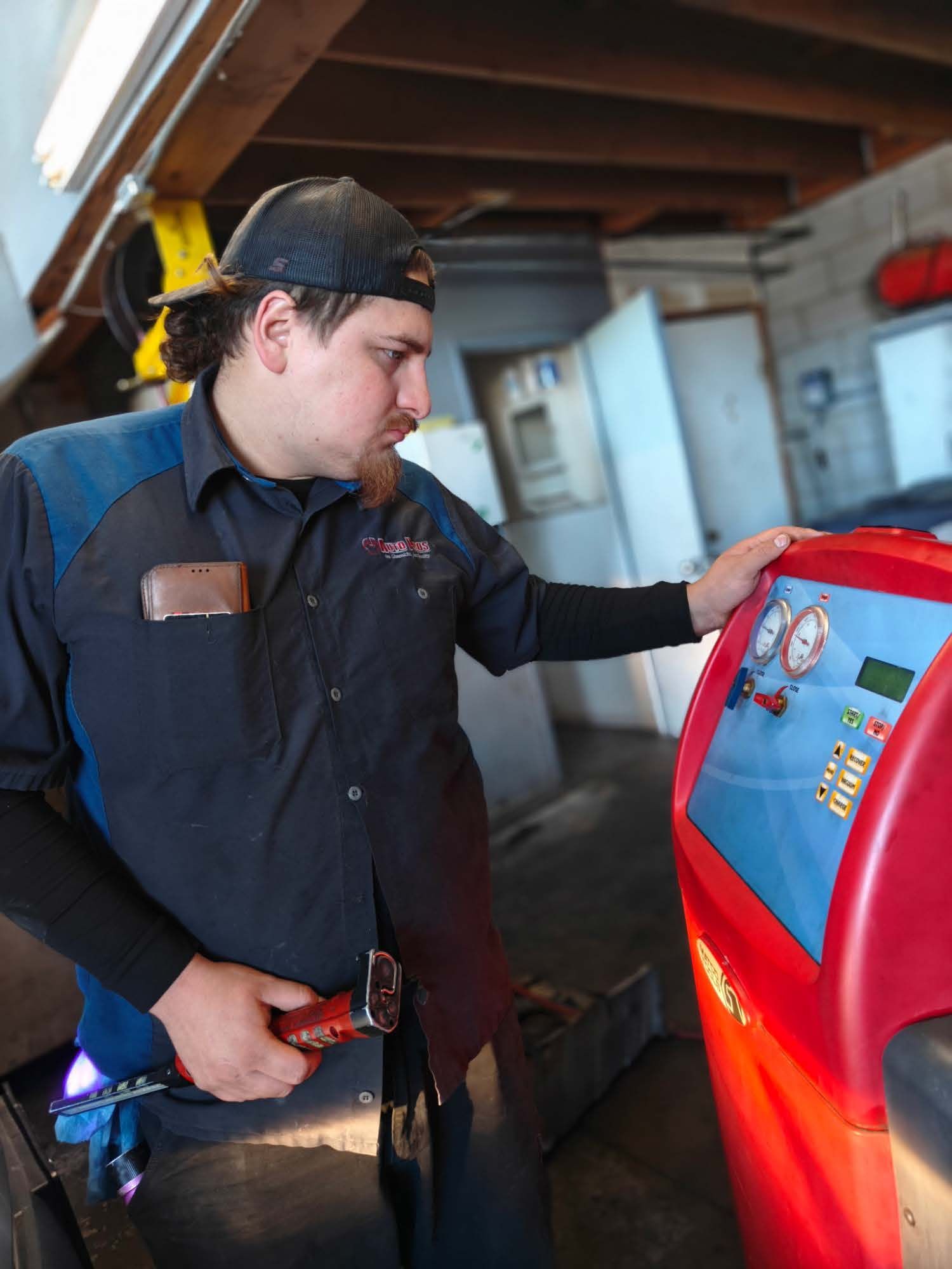 Worker in dark uniform inspecting a red machine in a garage workshop. | Auto Pros