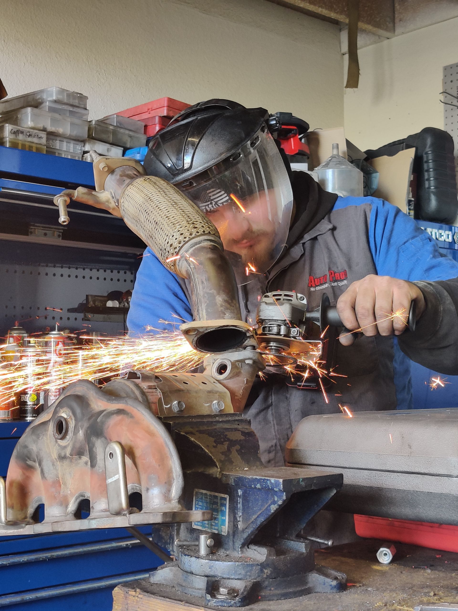 Welder grinding metal in a workshop, with bright sparks flying and tools on a bench. | Auto Pros