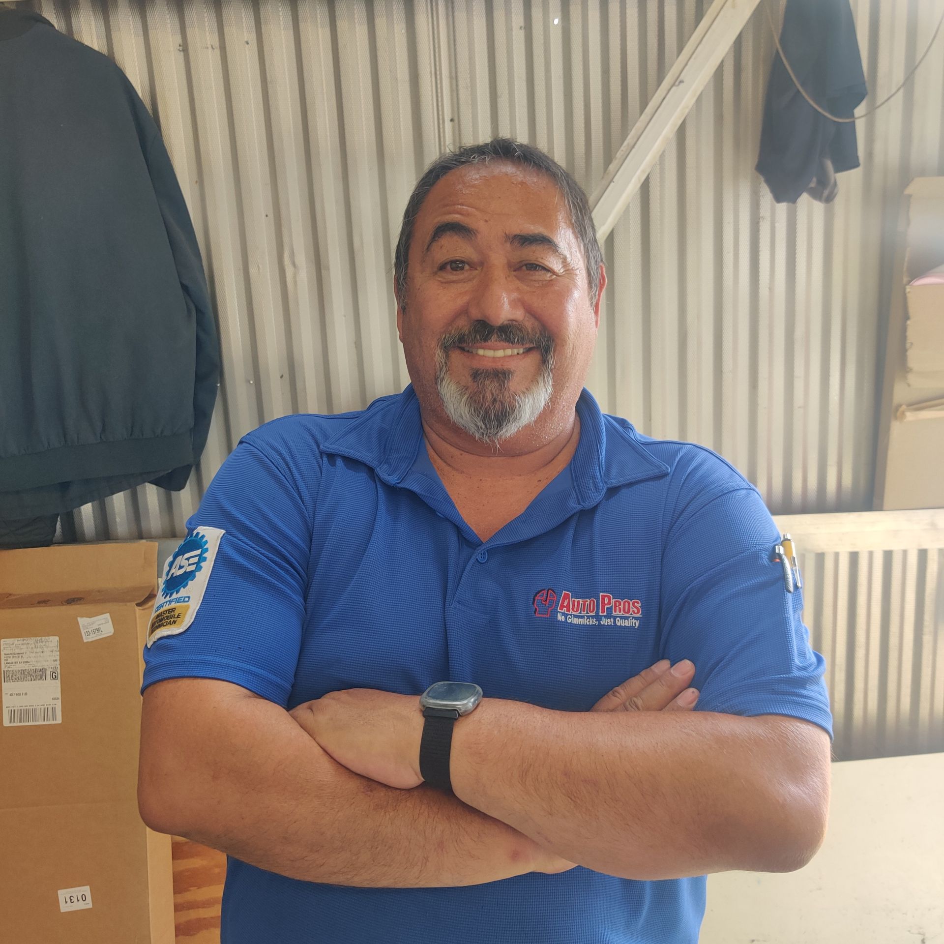 Man in blue polo shirt with arms crossed, standing in a corrugated metal workshop. | Auto Pros