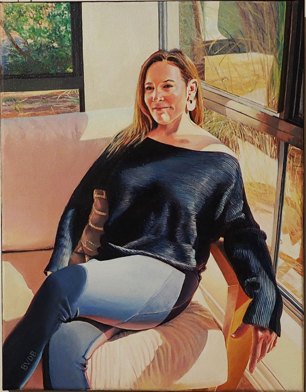A portrait of a person sitting on a sofa in a sunlit room, wearing a dark blue sweater and light blue jeans.