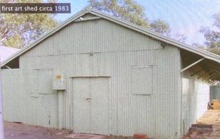 A light green, corrugated metal shed with a peaked roof and double doors, labeled 