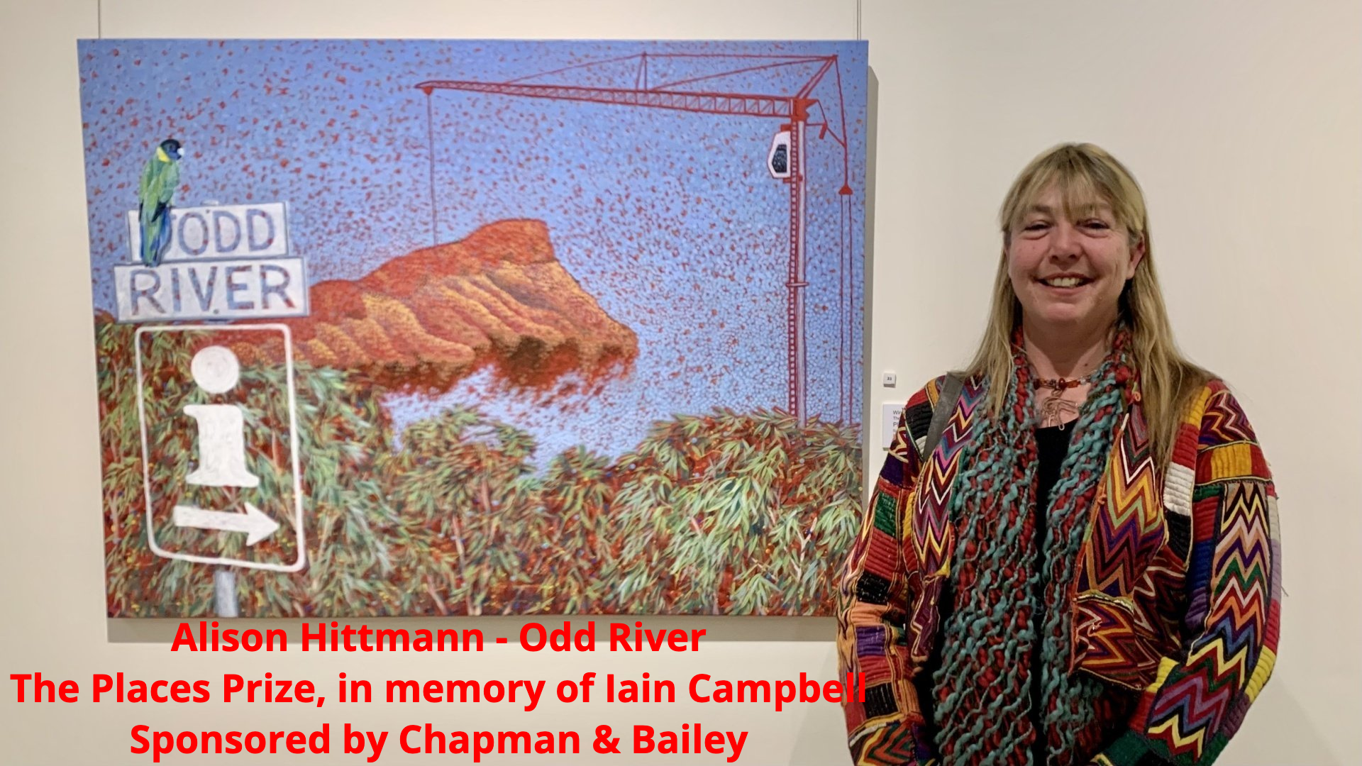 A person stands smiling beside their painting titled