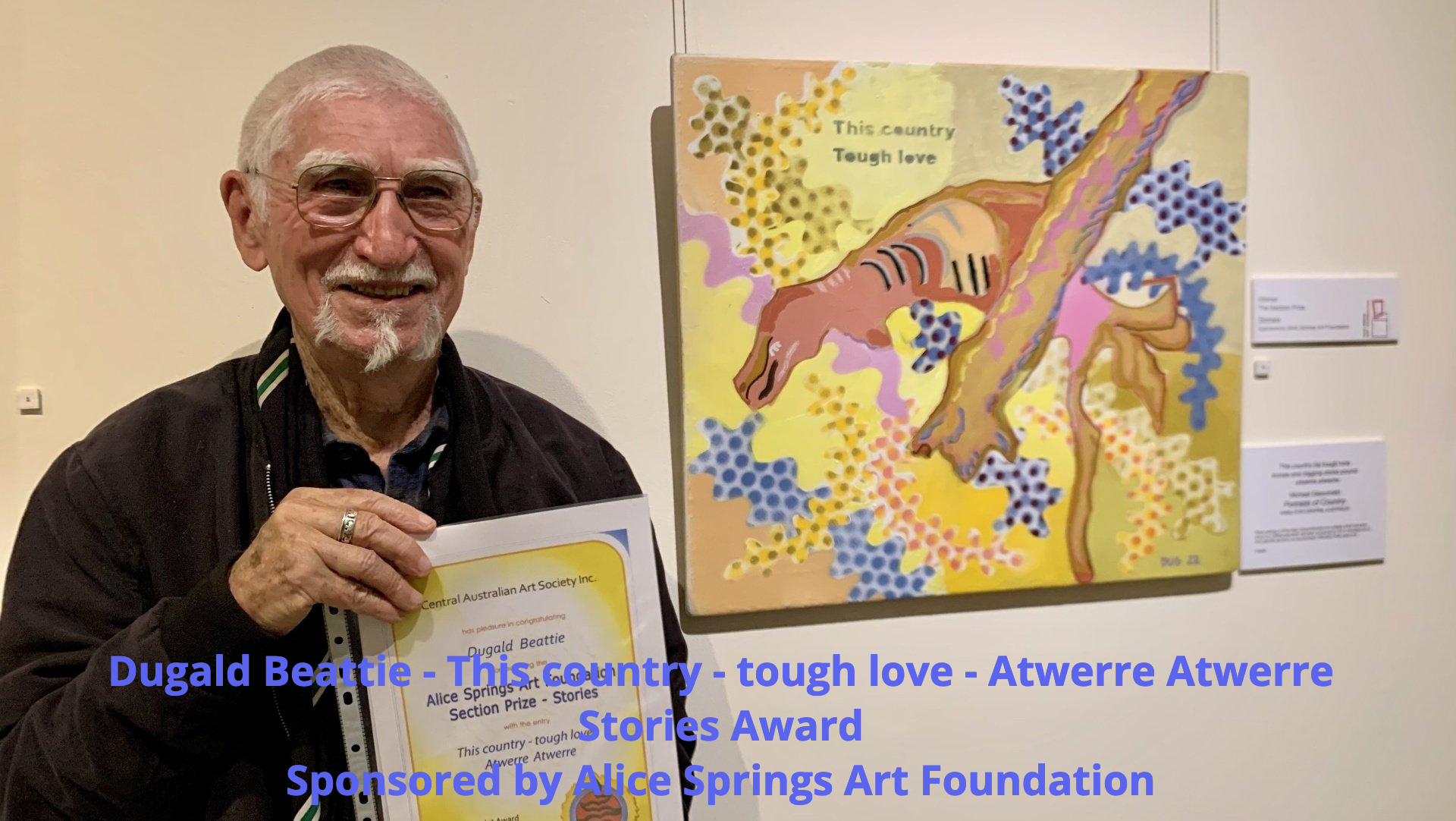 A man holding an award certificate stands next to his painting titled