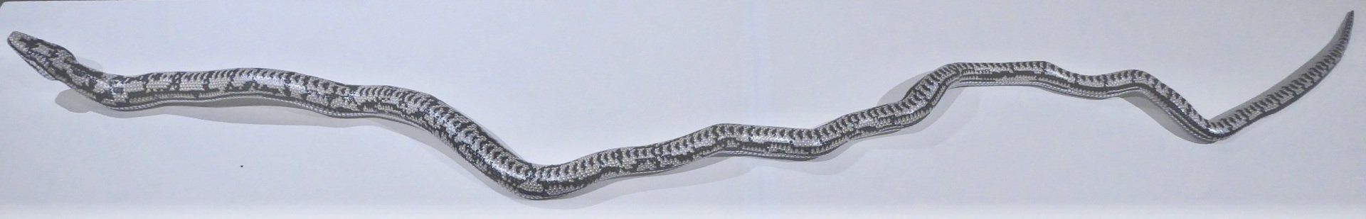 A thin, winding, silver-toned bracelet or chain featuring rectangular, textured links on a light background.