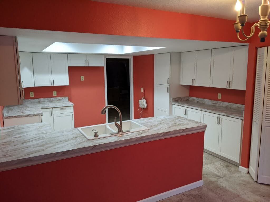 Empty kitchen with red walls, white cabinets, and a marble island with a sink and faucet