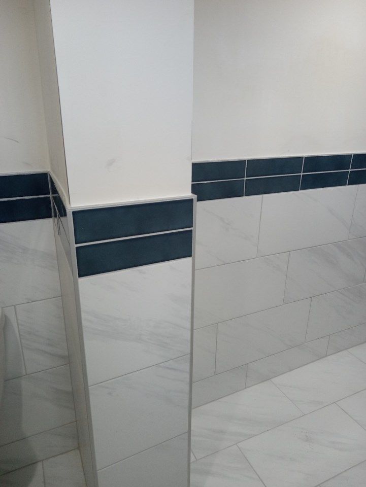 White tiled bathroom with dark blue horizontal accent strip and a corner pillar.