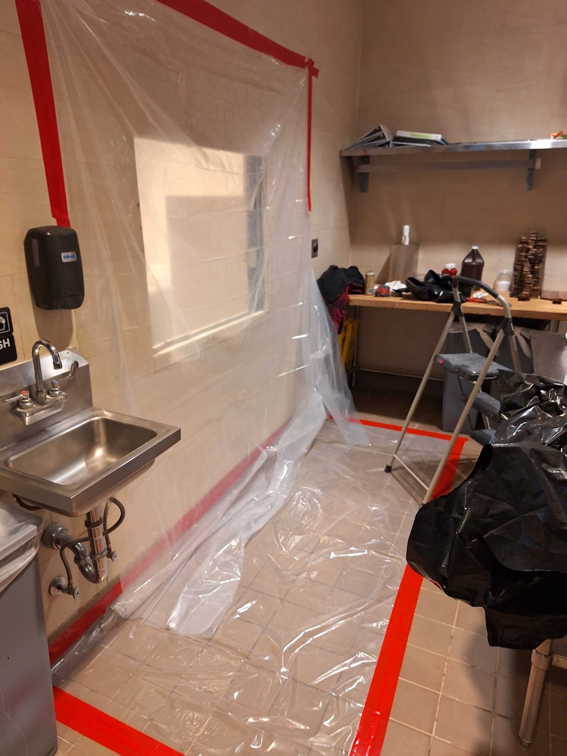 Plastic-covered room with sink, desk, and taped-off area during renovation or cleanup