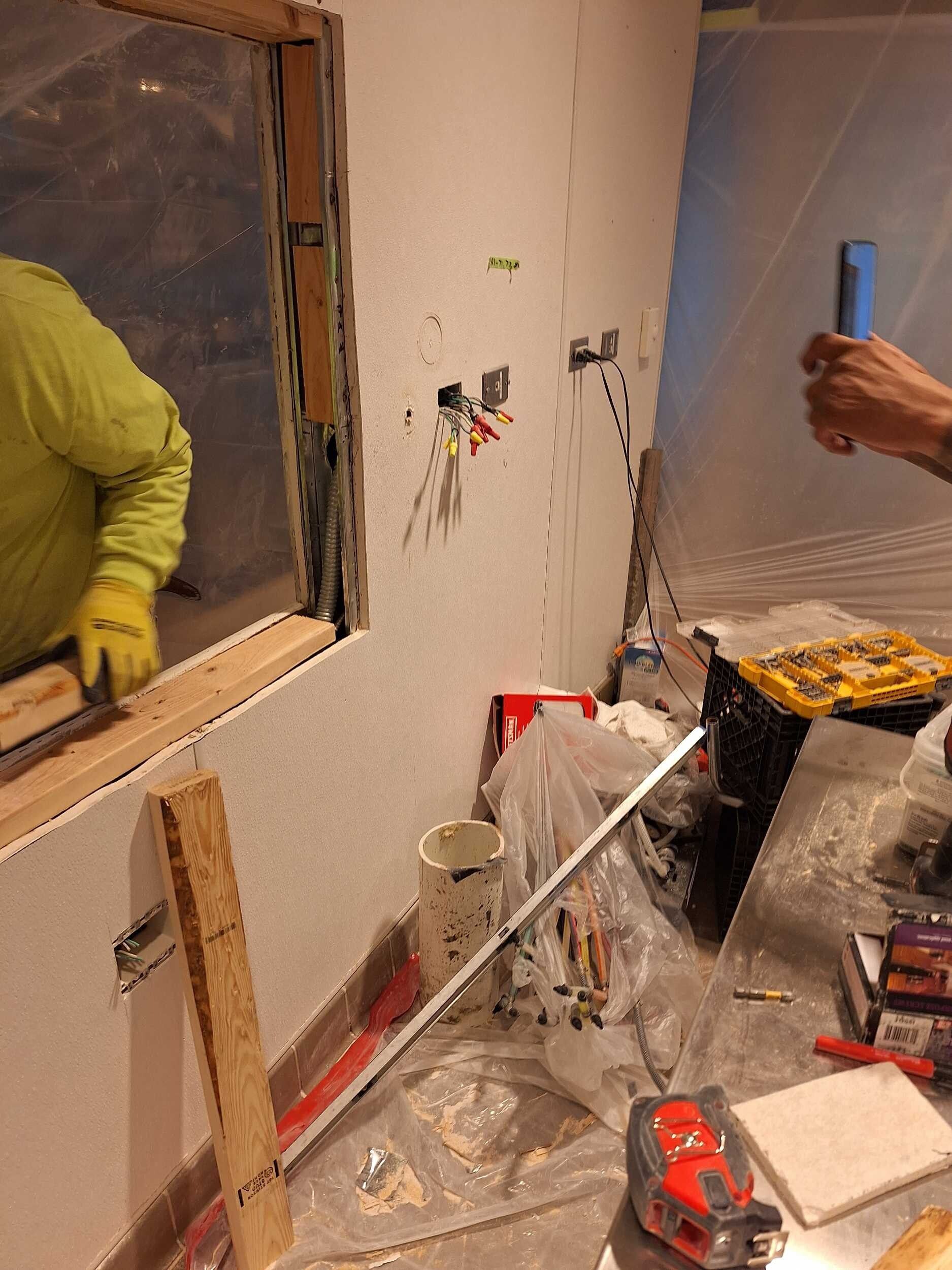 Bathroom under renovation with exposed wall, tools, paint bucket, and workers partially visible.