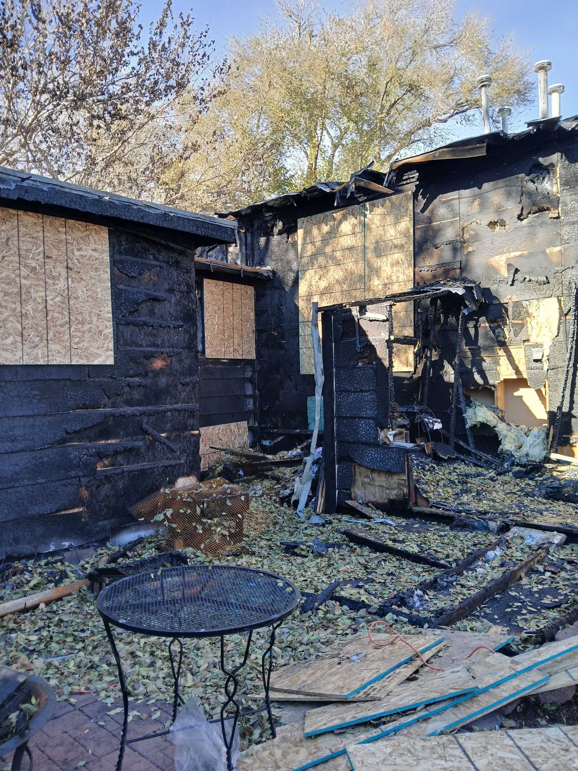 Charred remains of a house and backyard after a fire, with a small metal table in the foreground.