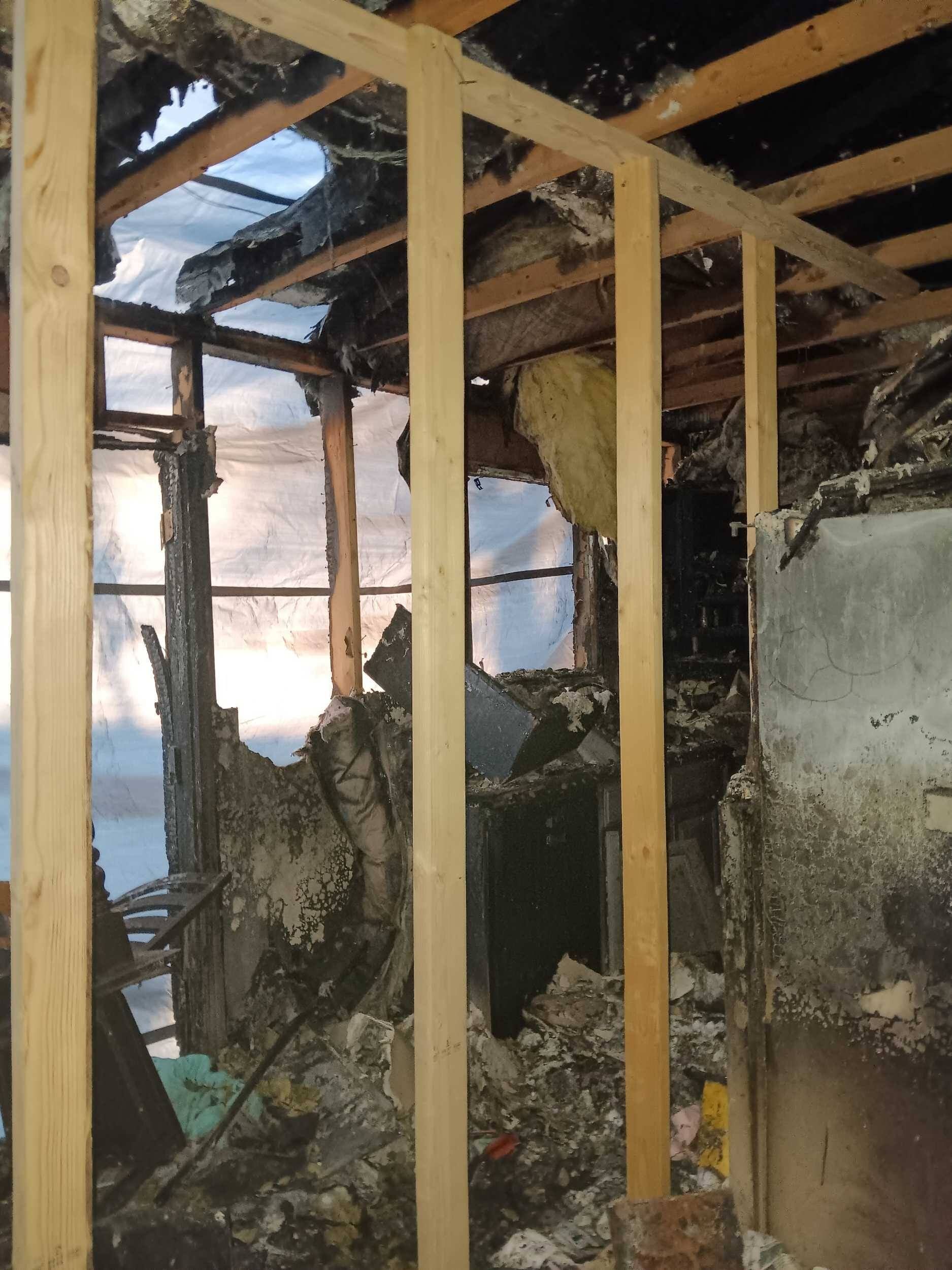 Charred interior of a damaged building with exposed wooden studs and burned walls after a fire