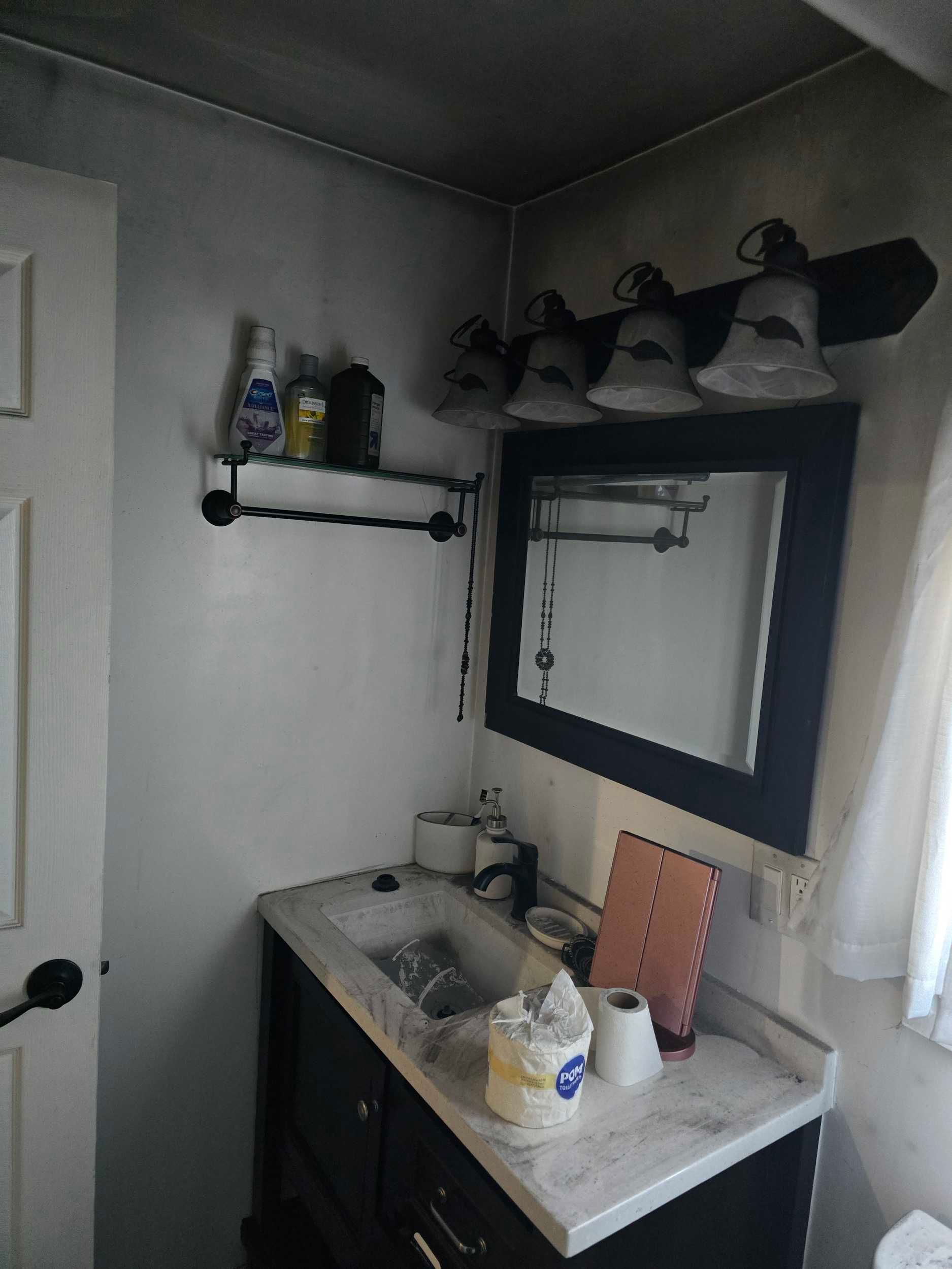 Small bathroom vanity with sink, mirror, shelves, and toiletries in a narrow, dimly lit room.