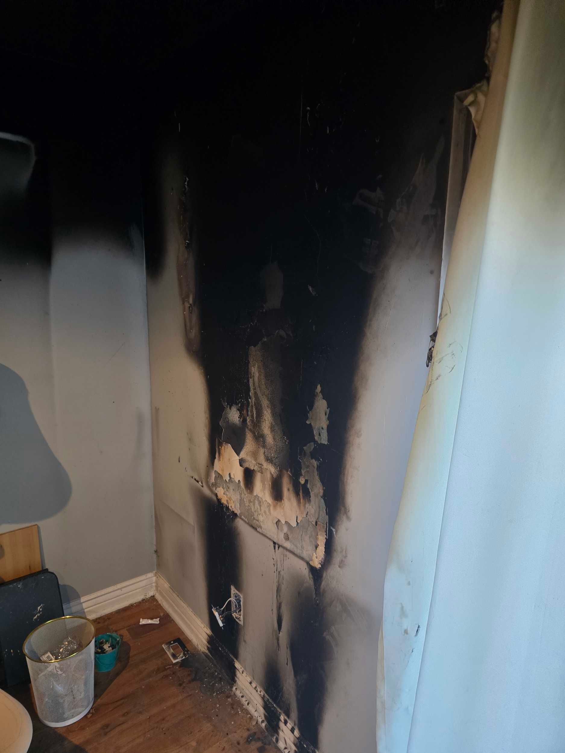 Charred wall with heavy smoke damage in a room, dark soot stains rising from the floor to the ceiling.