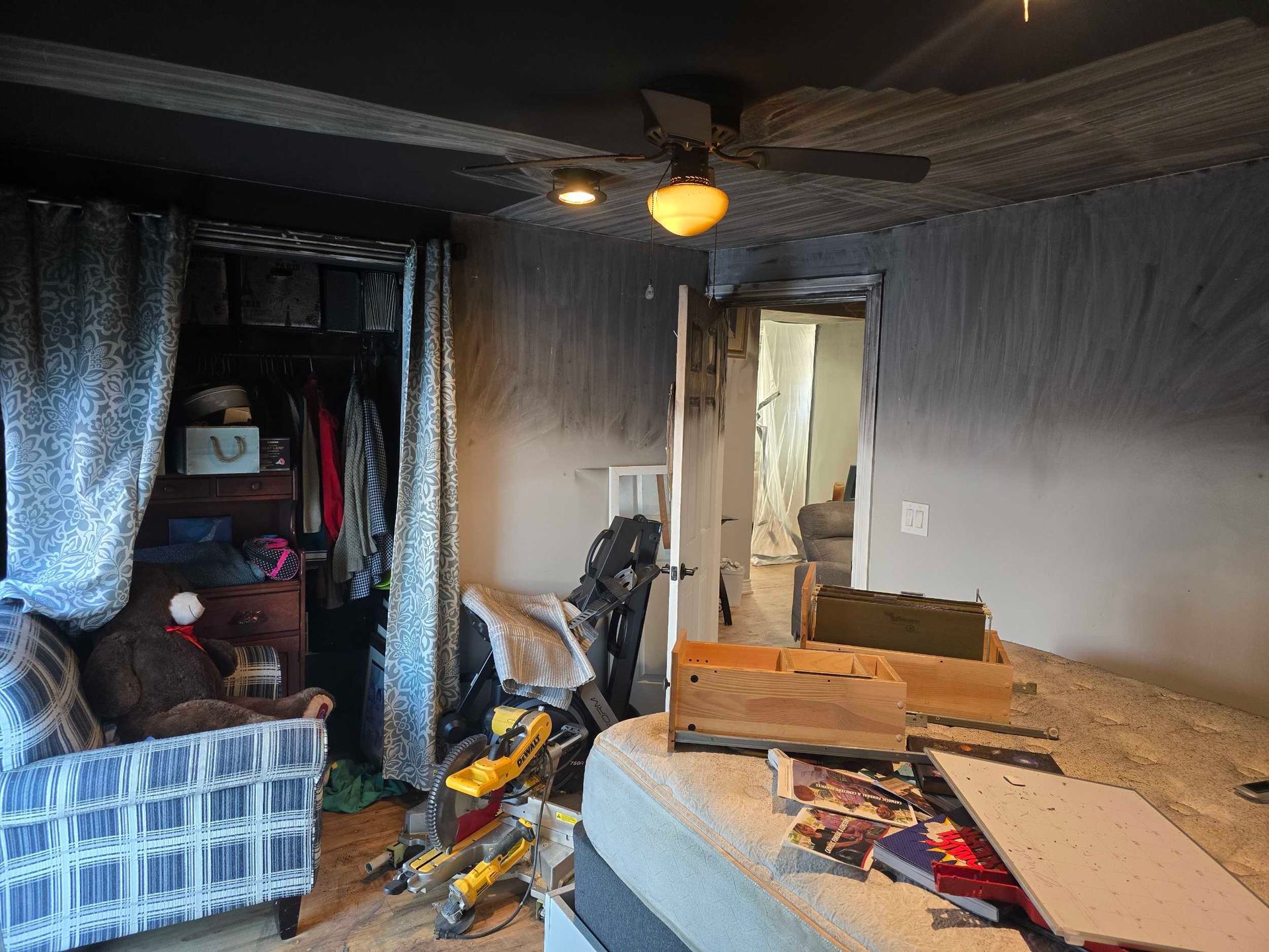 Messy living room with a bed, fan, boxes, and cluttered furniture after damage or renovation