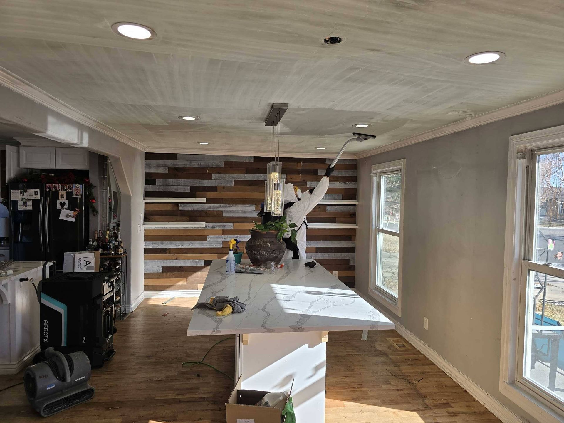 Bright room with a long table, wooden accent wall, windows, and a hanging light fixture.