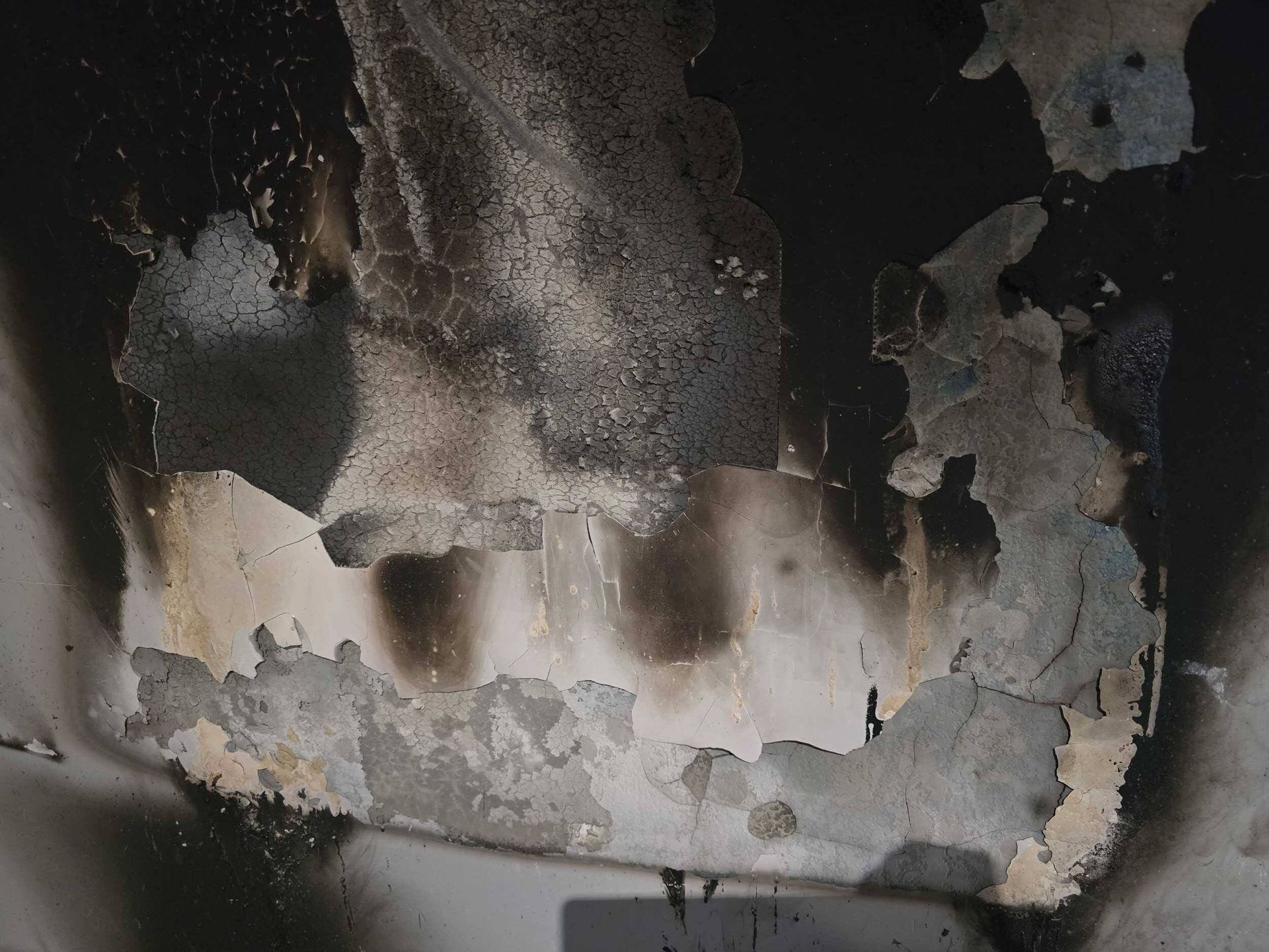 Charred, peeling wall with soot-stained gray and black patches and exposed surface beneath