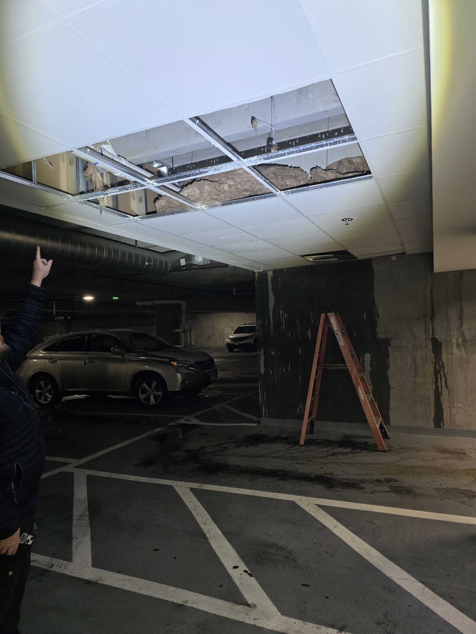 Parking garage ceiling with a large damaged opening and a ladder below it