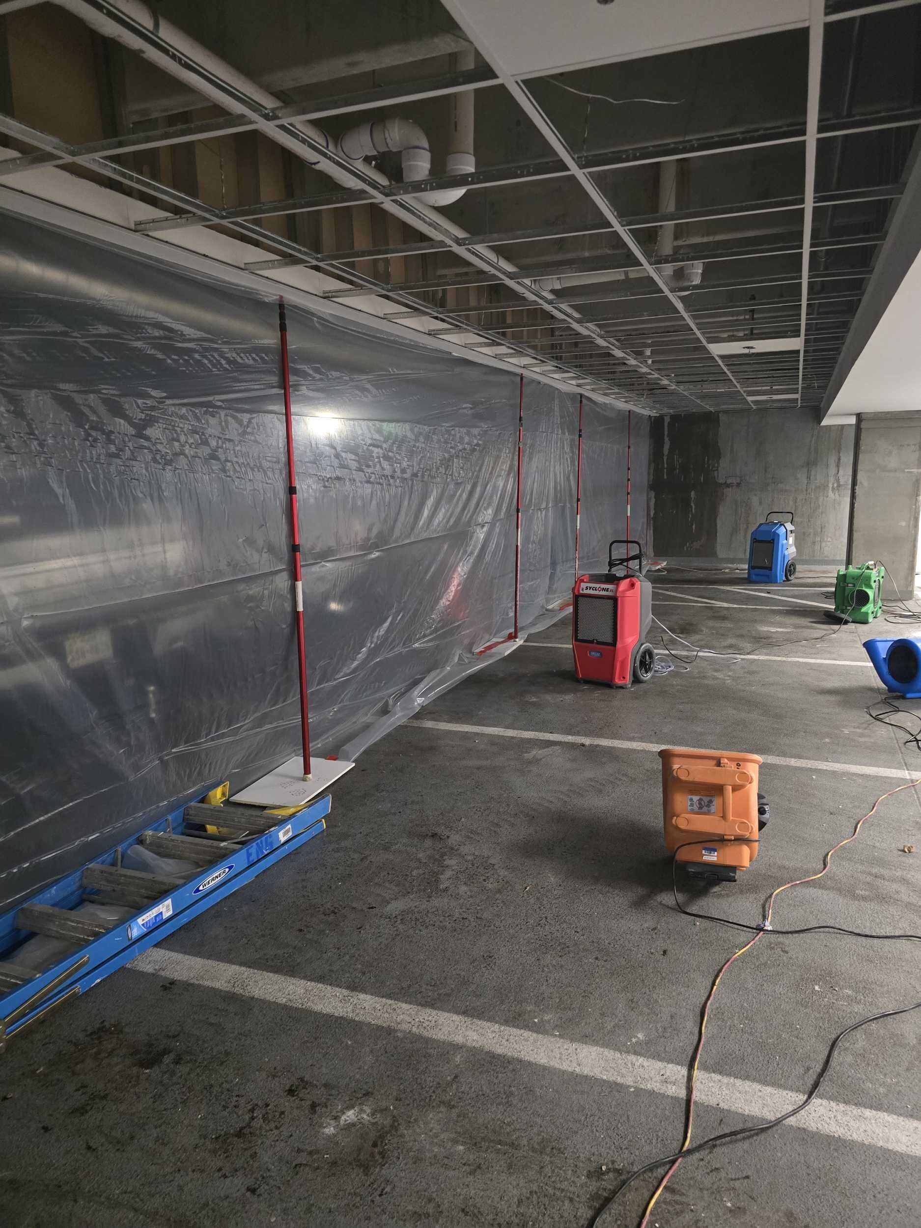 Interior construction site with plastic-covered wall, exposed ceiling, and scattered tools on the floor