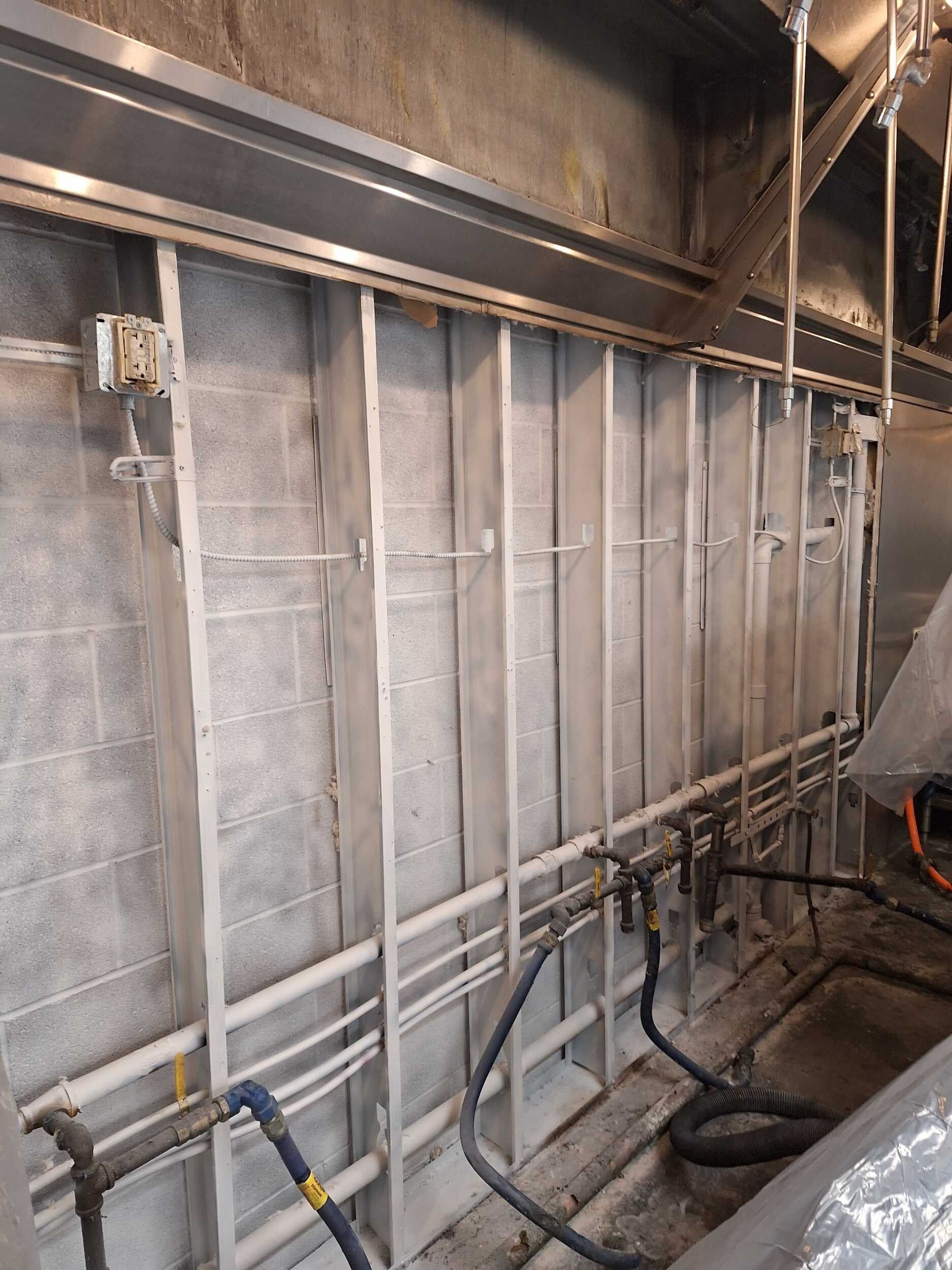 Industrial wall with exposed insulation, pipes, and cables in a maintenance area