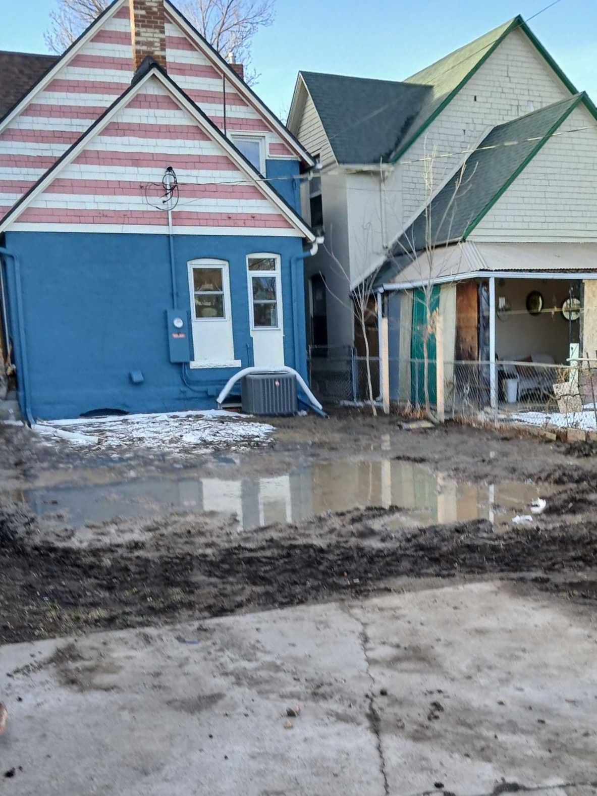 Flooded muddy street in front of two colorful houses with snow patches nearby